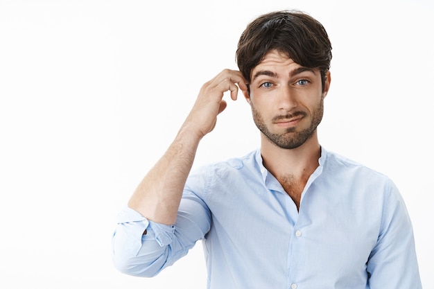 Portret van verward en geen idee, knappe vriend met blauwe ogen en baard kan hints vrouw niet begrijpen die grijnzend haar hoofd krabt terwijl ze naar voren wordt ondervraagd over grijze muur