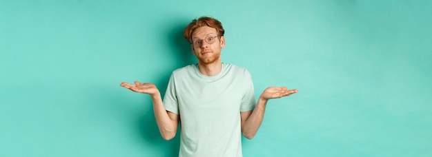 Portret van verwarde roodharige man in t-shirt en bril weten niets schouderophalend en kijkend