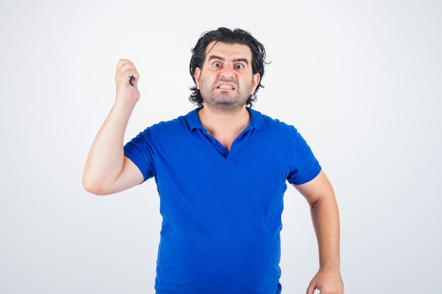 Portret van volwassen man dreigt met een schaar, tanden op elkaar klemmen in blauw t-shirt en op zoek agressief vooraanzicht