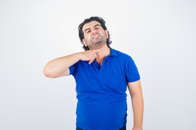 Portret van volwassen man gebaren met wijsvinger naar zijn nek alsof hij keel in blauw t-shirt doorsnijdt en agressief vooraanzicht kijkt