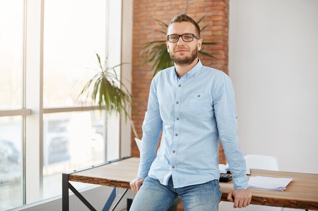 Portret van volwassen mannelijke freelance ontwerper in glazen en casual kleding, permanent in moderne co-werkruimte