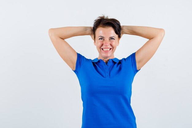 Portret van volwassen vrouw hand in hand achter hoofd in blauw t-shirt en op zoek gelukkig vooraanzicht