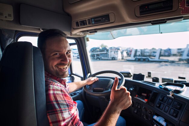 Portret van vrachtwagenchauffeur zitten in zijn vrachtwagen met duimen omhoog