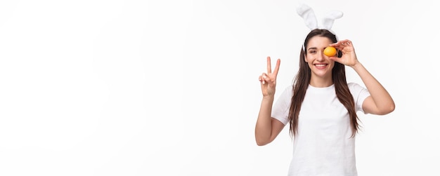 Portret van vreedzame en vrolijke jonge schattige vrouw in witte t-shirt showint vredesteken en colo vasthouden