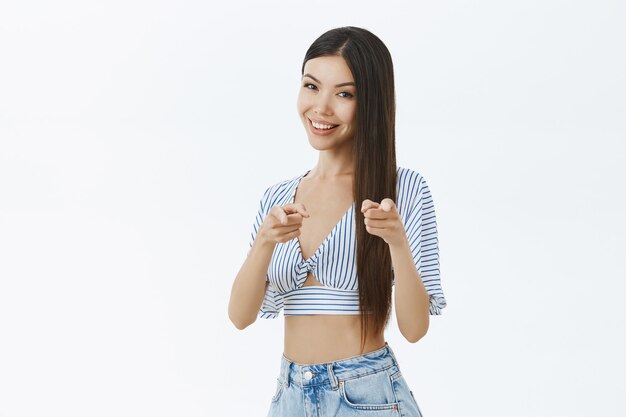Portret van vriendelijke uitgaande en zelfverzekerde jonge Aziatische vrouwelijke ondernemer in bijgesneden blouse wijzen