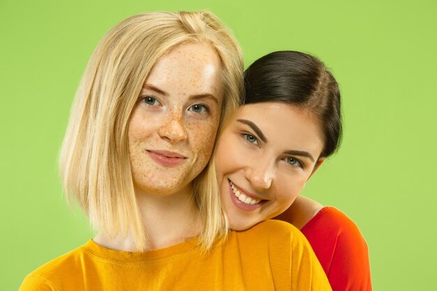 Portret van vrij charmante meisjes in casual outfits geïsoleerd op groene studio achtergrond. Twee vrouwelijke modellen als vriendinnen of lesbiennes. Concept van LGBT, gelijkheid, menselijke emoties, liefde, relatie.