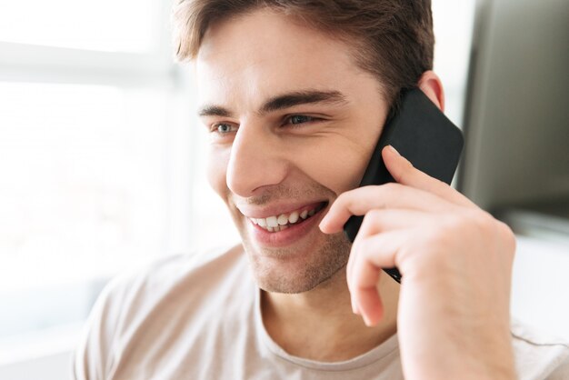 Portret van vrolijke aantrekkelijke man praten over telefoon thuis