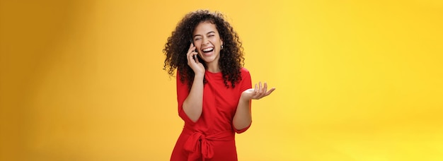 Portret van vrolijke charmante europese vrouw in rode jurk met krullend haar hardop lachend als roddels