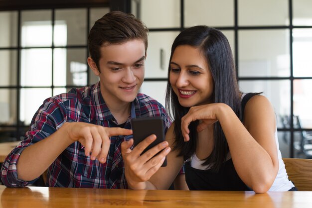 Portret van vrolijke studentenvrienden die op smartphone doorbladeren