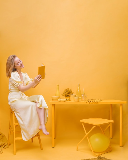 Gratis foto portret van vrouw die een boek in een gele scène leest