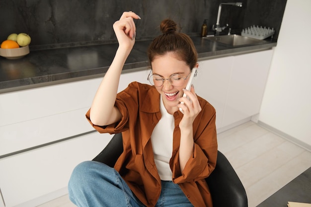 Portret van vrouw die geweldig nieuws ontvangt via het telefoontje viert en springt op de stoel van