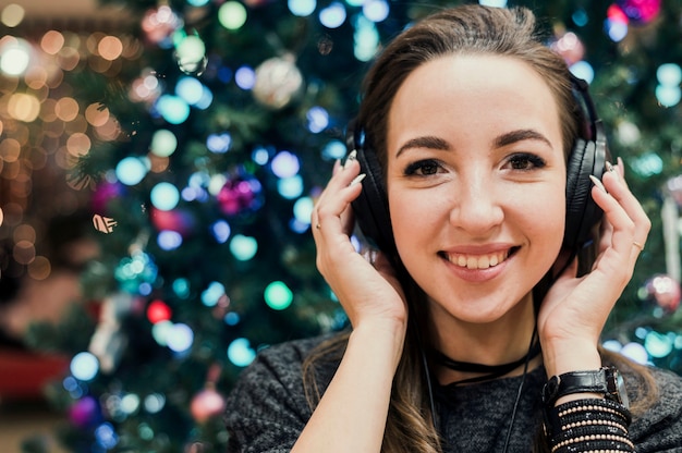 Gratis foto portret van vrouw die hoofdtelefoons draagt dichtbij kerstmisboom
