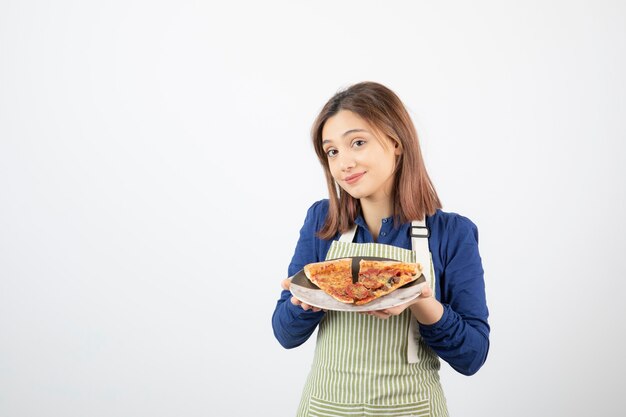 Portret van vrouw in keukenschort die plaat van pizza op wit toont