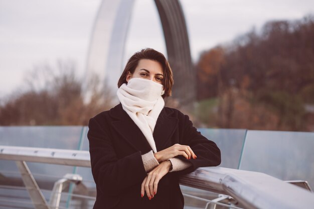Portret van vrouw in zwarte winterjas en witte sjaal op stadsplein.