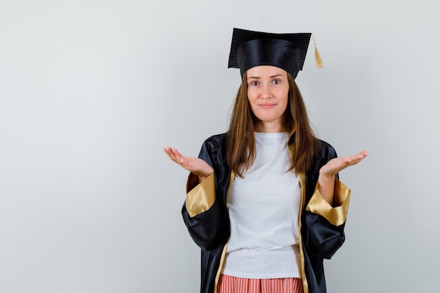 Portret van vrouwelijke afgestudeerde die hulpeloos gebaar in uniforme, vrijetijdskleding toont en aarzelend vooraanzicht kijkt