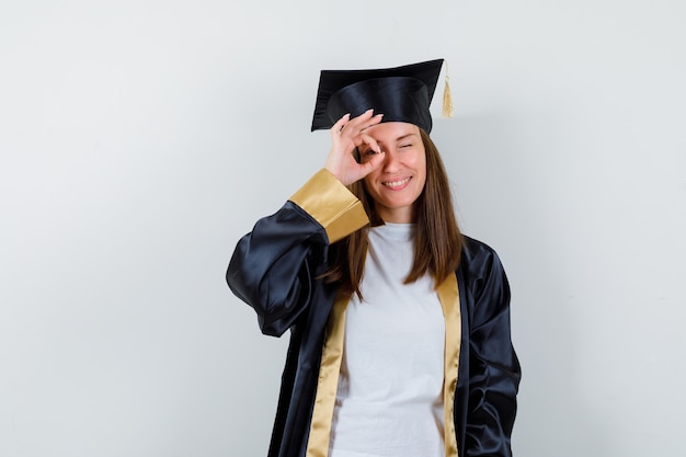 Portret van vrouwelijke afgestudeerde ok teken tonen op oog in jurk, vrijetijdskleding en op zoek naar zelfverzekerd vooraanzicht