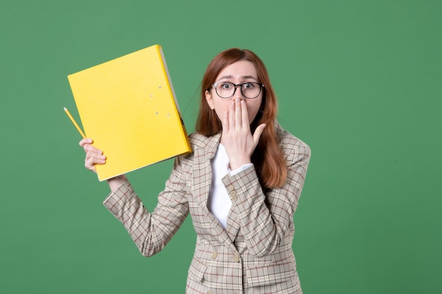 Portret van vrouwelijke leraar die geel document op groen houdt