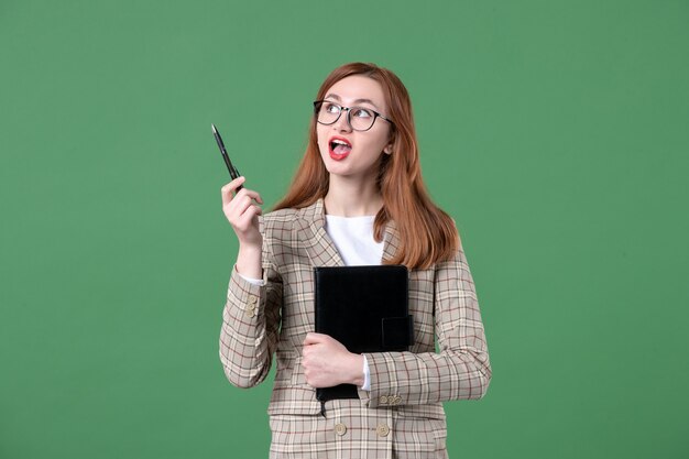 Portret van vrouwelijke leraar in pak met notitieblok op groen