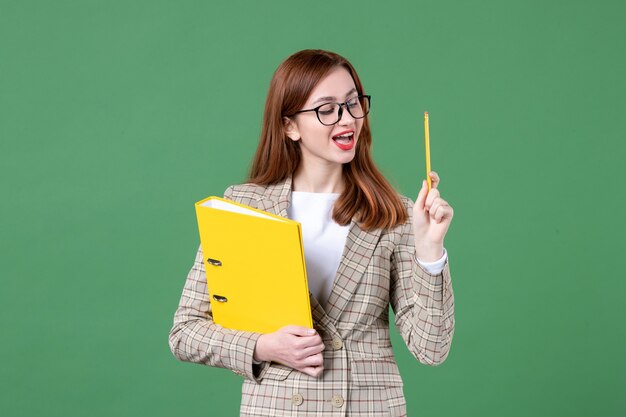 Portret van vrouwelijke leraar met gele bestanden en potlood op groen