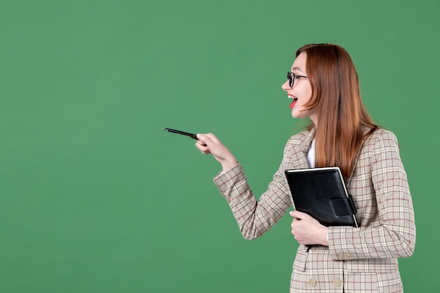 Portret van vrouwelijke leraar met notitieblok in gesprek met iemand op groen