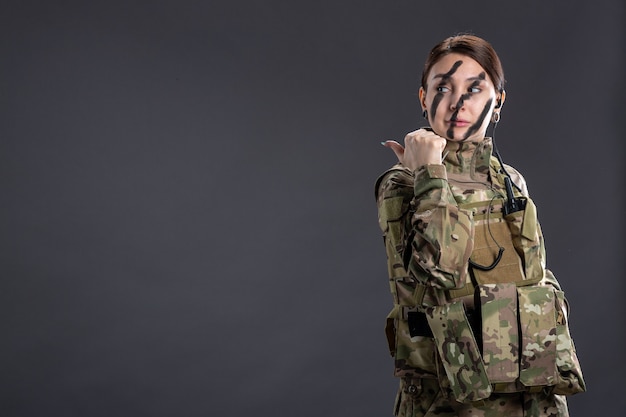 Portret van vrouwelijke soldaat in camouflage op de donkere muur