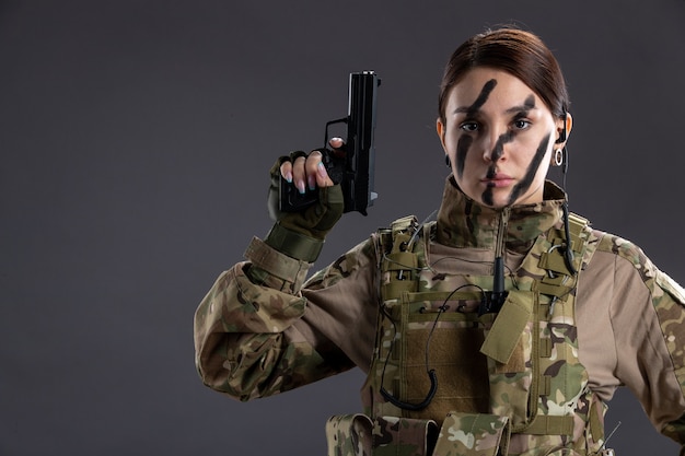 Portret van vrouwelijke soldaat in militair uniform met pistool op de donkere muur