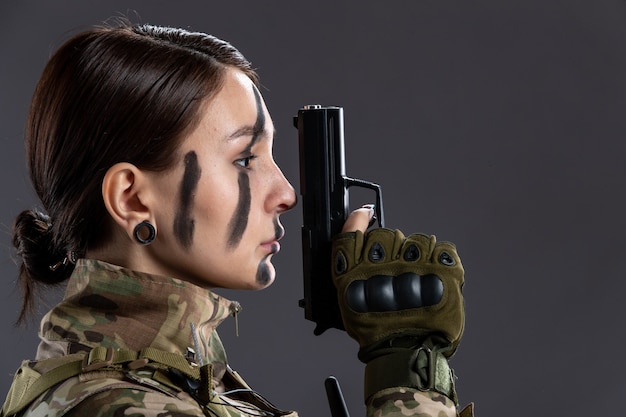 Portret van vrouwelijke soldaat in militair uniform met pistool op de donkere muur