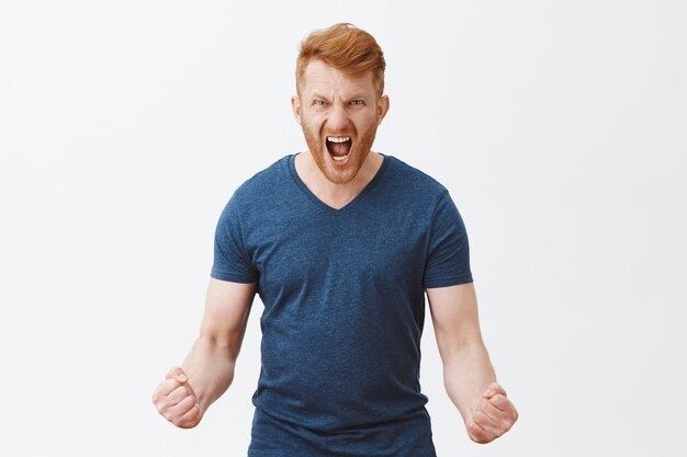 Portret van woedende, boze en pissige sterke mannelijke roodharige man met borstelharen, gebalde vuisten in woede, schreeuwen, rimpelige neus, woedend op het punt iemand te slaan