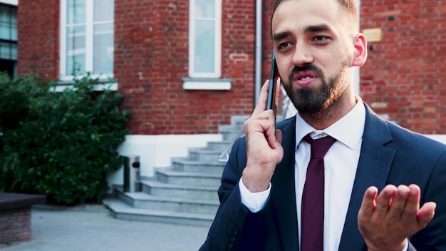 Portret van zakenman in diplomatiek pak die buiten voor het kantoor van het opstartende bedrijf staat en aan de telefoon praat over financiële strategie met externe manager. Buiten concept