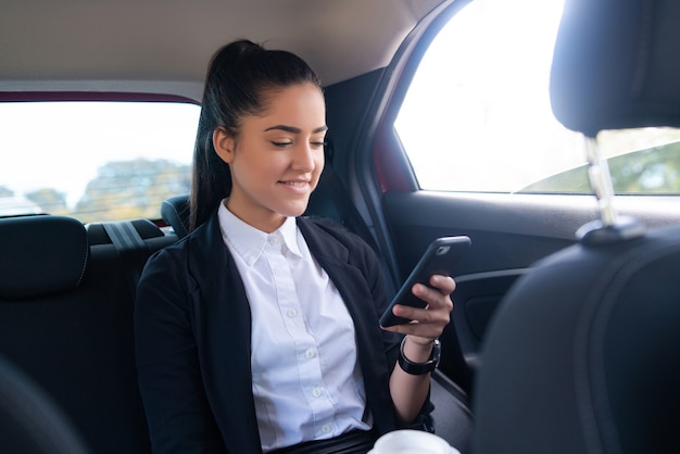 Portret van zakenvrouw met behulp van haar mobiele telefoon op weg naar het werk in een auto. Bedrijfsconcept.