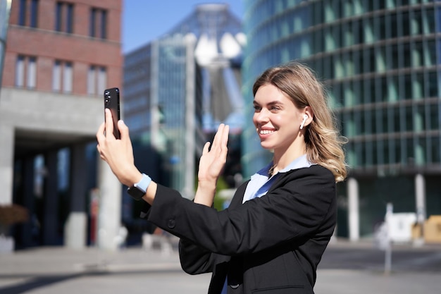 Portret van zakenvrouw zwaait met haar hand naar de camera van de mobiele telefoon zwaait met de hand tijdens videochatstands i