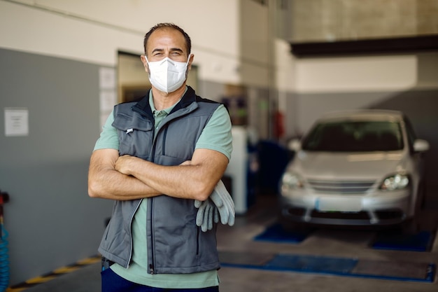 Portret van zelfverzekerde automonteur met gezichtsmasker in zijn reparatiewerkplaats