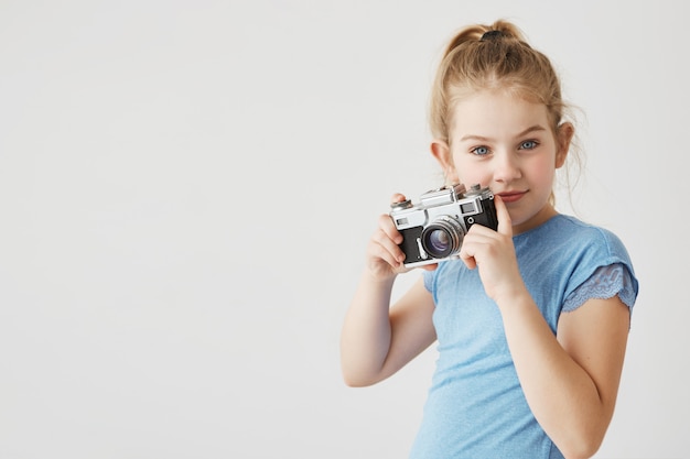 Portret van zelfverzekerde jonge dame met blauwe ogen en blond haar poseren met haar fotocamera laten zien dat ze fotograaf wil worden. Kopieer ruimte