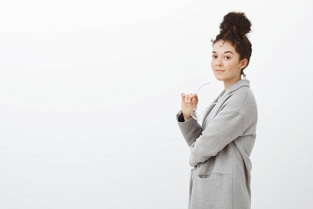 Portret van zelfverzekerde succesvolle zakenvrouw in grijze trendy jas, permanent in profiel en glimlachend zelfverzekerd, bril in de hand houden, in de metro naar het werk gaan