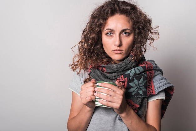 Portret van zieke de koffiemok van de vrouwenholding tegen grijze achtergrond
