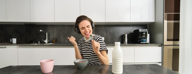 Gratis foto portret van zorgeloze brunette vrouw die haar ontbijtgranen eet, naar muziek luistert en ontbijt in de