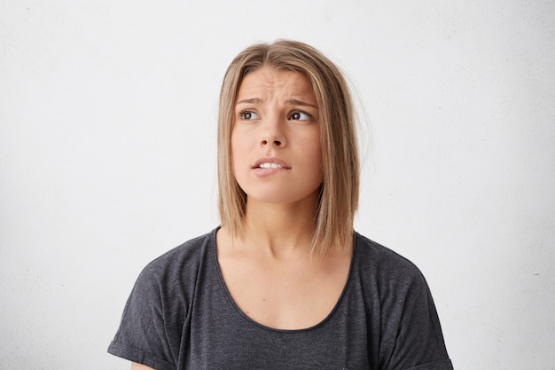 Gratis foto portret van zwaarhartige jonge dame die met agitatie opzij kijkt die haar lippen bijt.