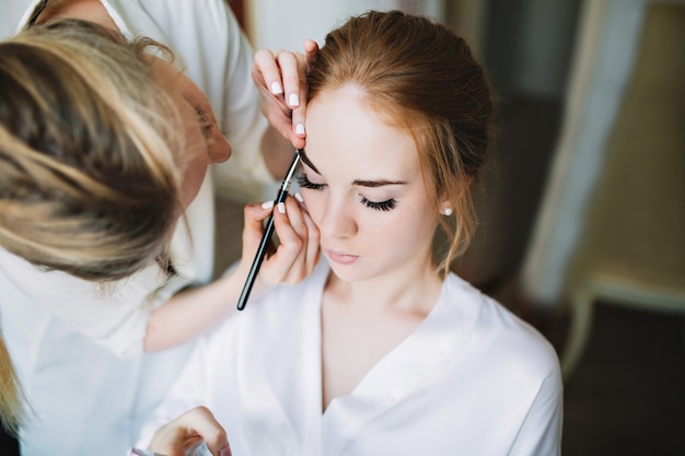 Portretvoorbereiding van bruid in de ochtend voor huwelijk. Kunstenaar maakt make-up en ze houdt haar ogen gesloten