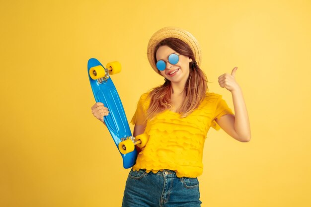 Poseren met skateboard. Het portret van de Kaukasische vrouw op gele studioachtergrond.