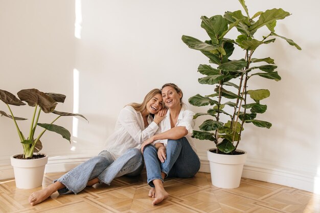 Positieve blanke blonde meisjes van verschillende leeftijden zitten op de vloer in een lege ruimte tegen een witte muur. Concept van genieten van weekend, vakantie