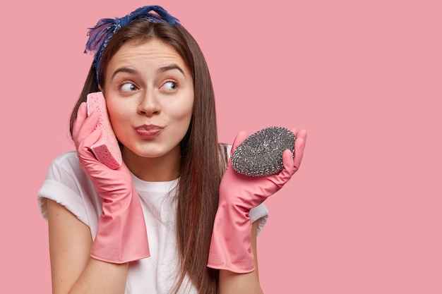 Gratis foto positieve blanke vrouw beweert te spreken op mobiele telefoon, houdt spons in de buurt van oor, gekleed in vrijetijdskleding