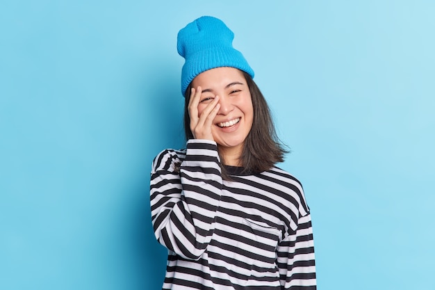 Positieve brunette schattig meisje met oosterse uitstraling bedekt gezicht met handglimlachen gelukkig