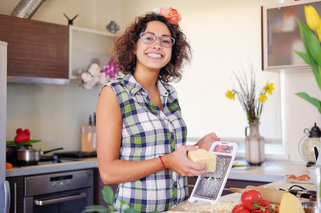 Positieve brunette vrouw met krullend haar maakt salade met tomaten en aardappel in een huiskeuken.