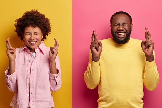 Positieve donkere huidskleurige vriendin en vriend kruisen vingers terwijl ze wensen, glimlachen gelukkig bidden voor geluk