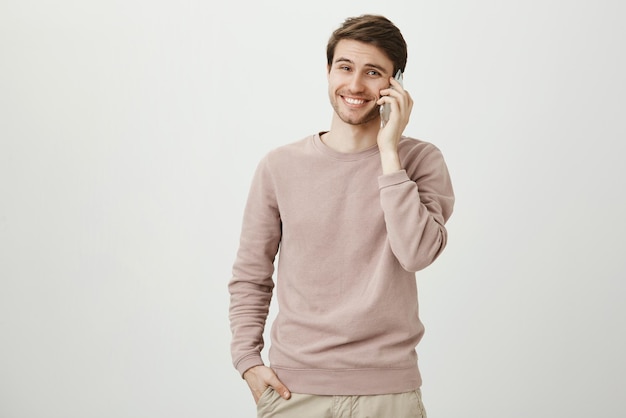 Positieve en knappe jonge blanke man met haren die lacht terwijl hij op smartphone praat
