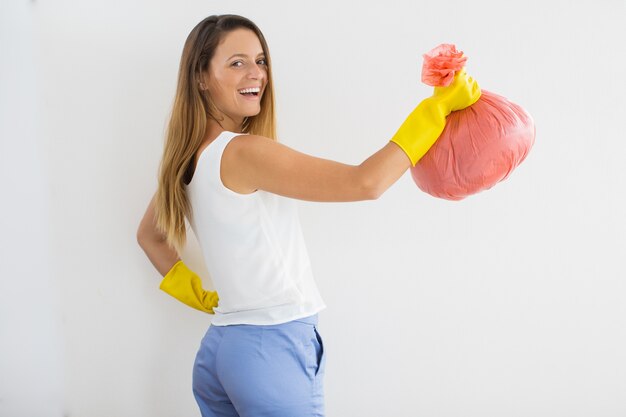 Positieve huisvrouw in rubberhandschoenen met vuilniszak