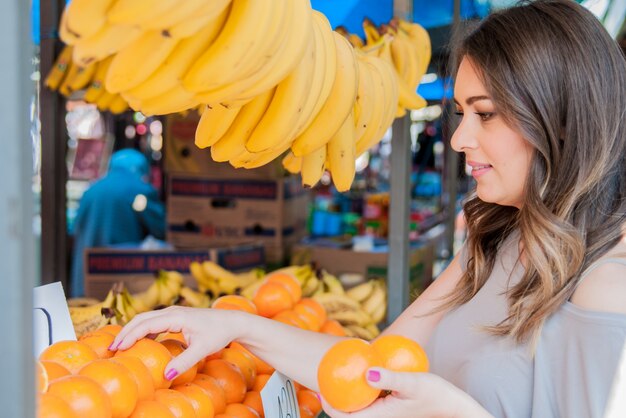 Positieve jonge vrouw die sinaasappels op de markt koopt. Vrouw kiezen sinaasappel