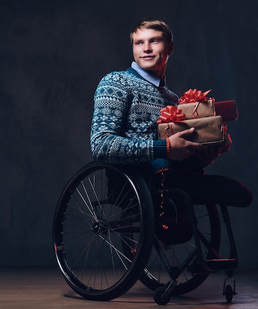 Positieve man in rolstoel met kerstcadeaus over donkergrijze achtergrond.