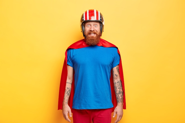 Gratis Foto positieve mannelijke superheld draagt helm, blauw t-shirt en mantel