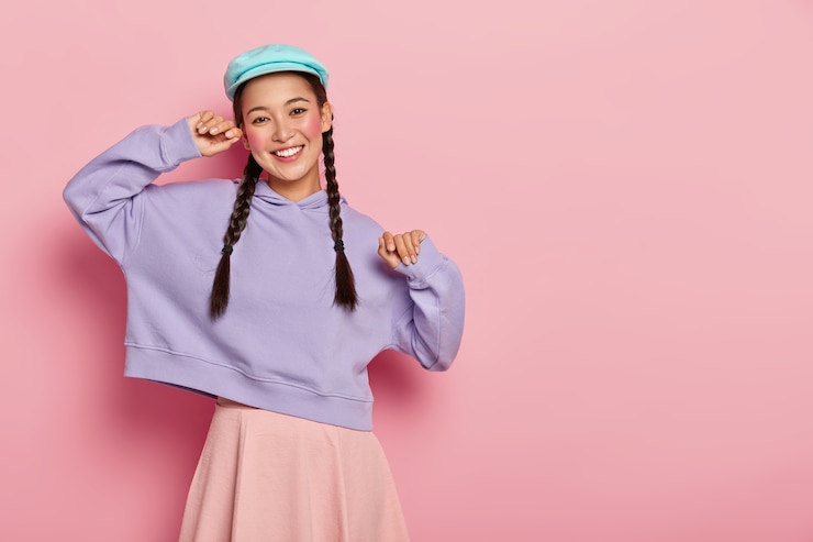 Gratis Foto positieve modieuze tienermeisje met make-up, stijlvolle pet, paarse sweater en rok draagt, in goed humeur is, komt op ontmoeting met groepsgenoten, geïsoleerd over roze muur